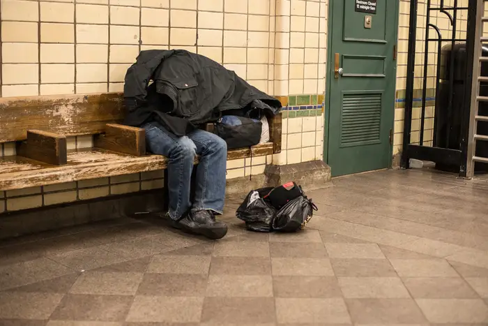 Homeless man sleeping on the bench in New York City subway station covered by own coat.